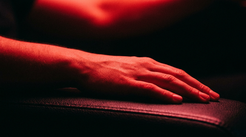 Hand en onderarm rusten onder fel rood licht tegen een donkere achtergrond