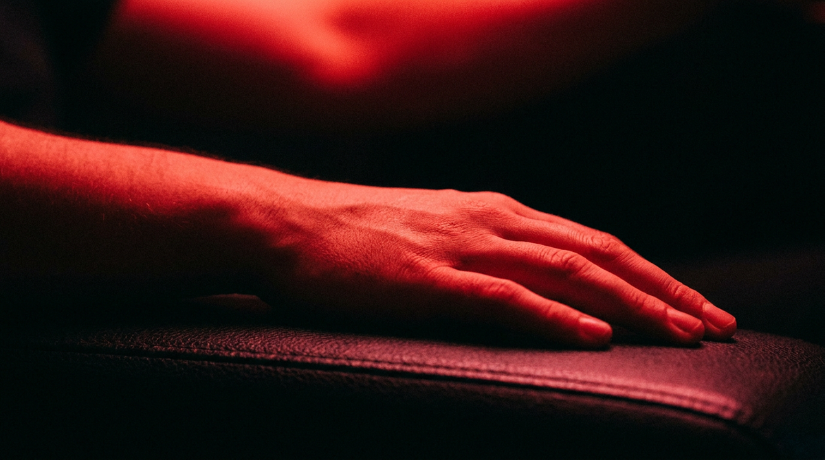 Hand en onderarm rusten onder fel rood licht tegen een donkere achtergrond